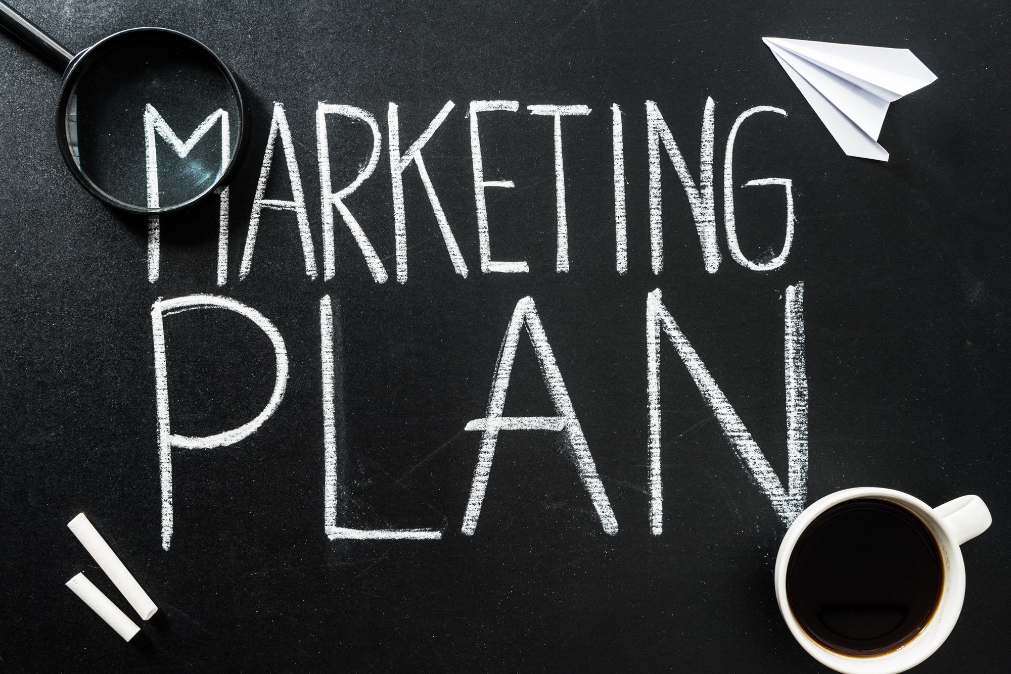 Top view of marketing plan lettering on chalkboard with cup of coffee and magnifier